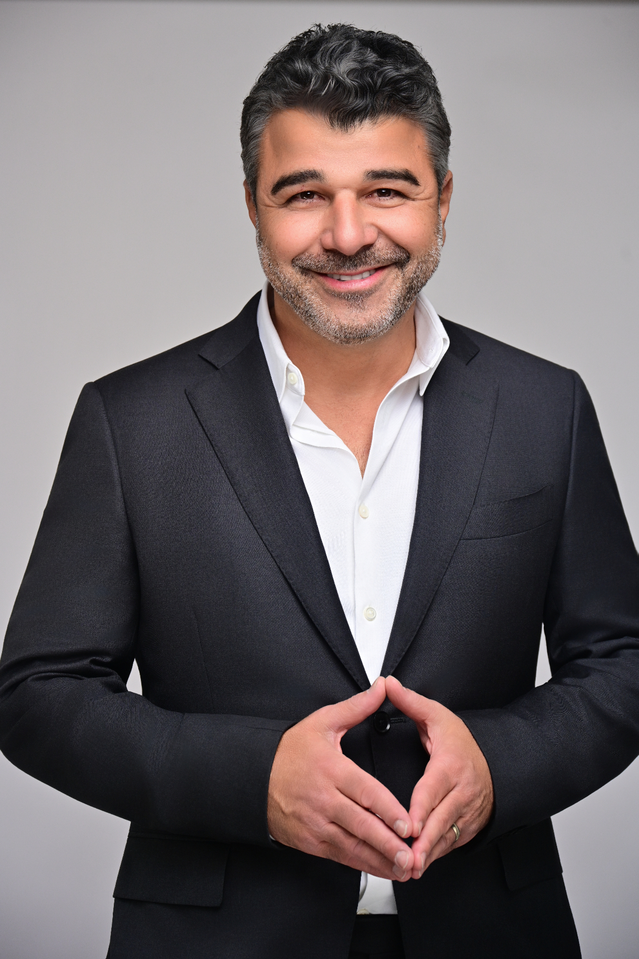 Studio corporate headshot of a man in a charcoal suit and open-collar white shirt