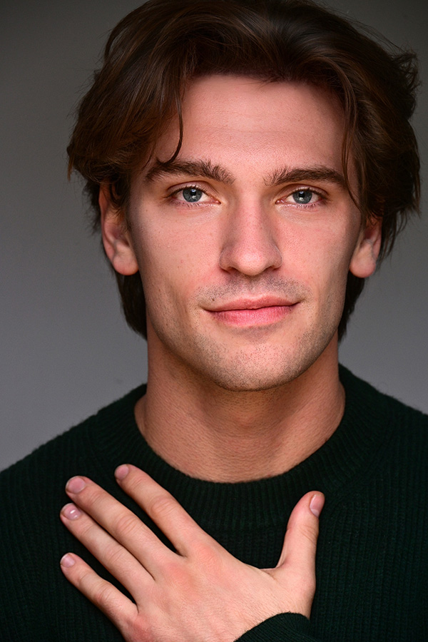 Young male actor headshot in green sweater with hand on chest, NYC by Dorothy Shi