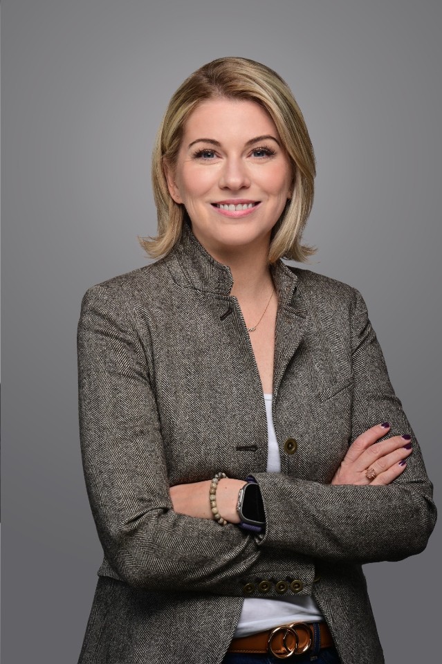Studio corporate headshot of a woman in a herringbone blazer, arms crossed