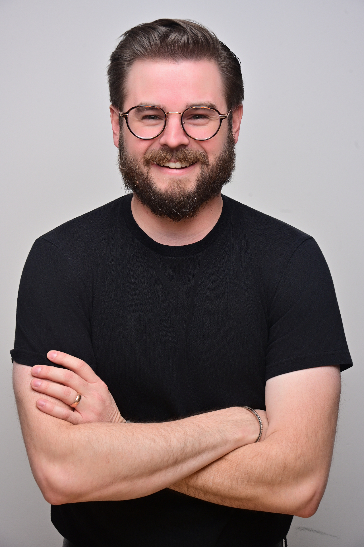 Studio corporate headshot of a man with glasses in a black shirt, arms crossed