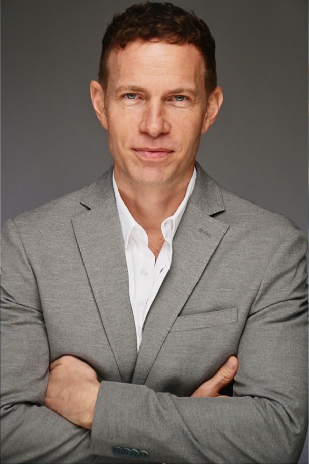 Corporate headshot of a man in a gray suit, arms crossed